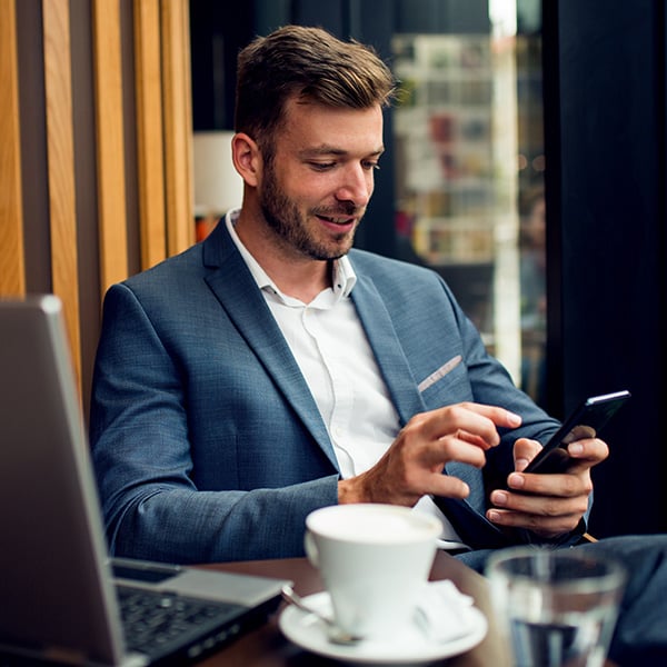 A man in a suit uses his smartphone in a cafe.